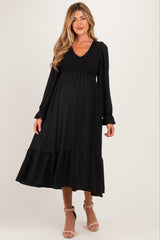 woman wearing a black maternity dress with puffed sleeves and a ruffled hem, showcasing her baby bump