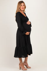 woman wearing a black maternity dress with a smocked bodice and ruffled hem, gently cradling her baby bump