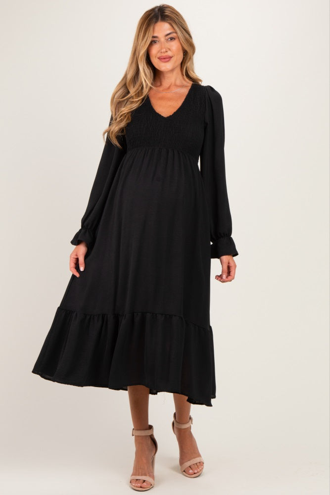 woman wearing a black maternity dress with puffed sleeves and a ruffled hem, showcasing her baby bump