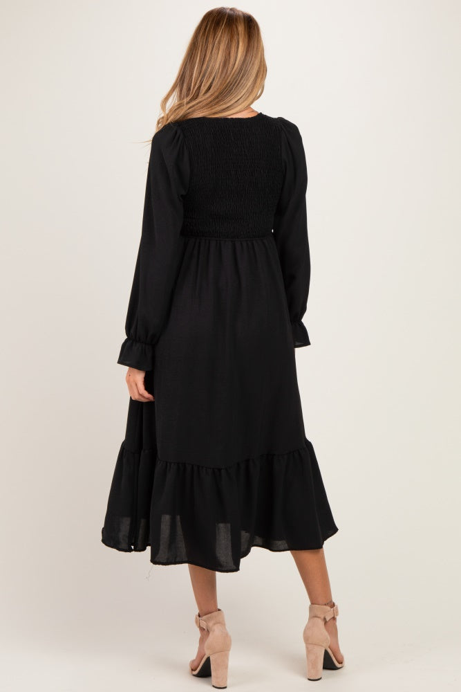 woman wearing a black maternity dress with long sleeves and a ruffled hem, showing the back view