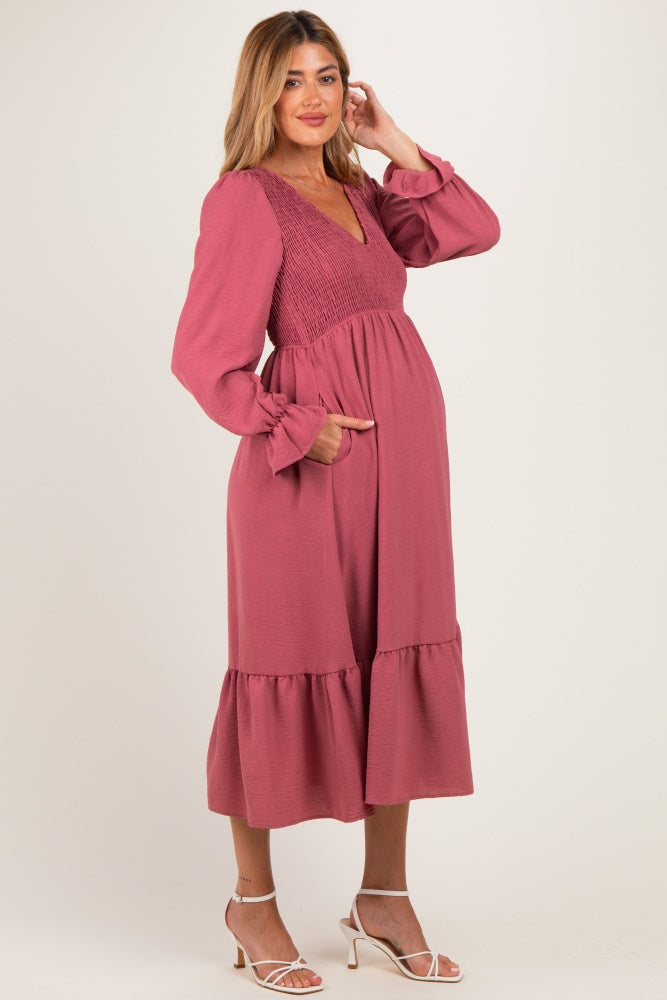 woman wearing a dusty rose maternity dress with smocked bodice and long sleeves, showing a baby bump