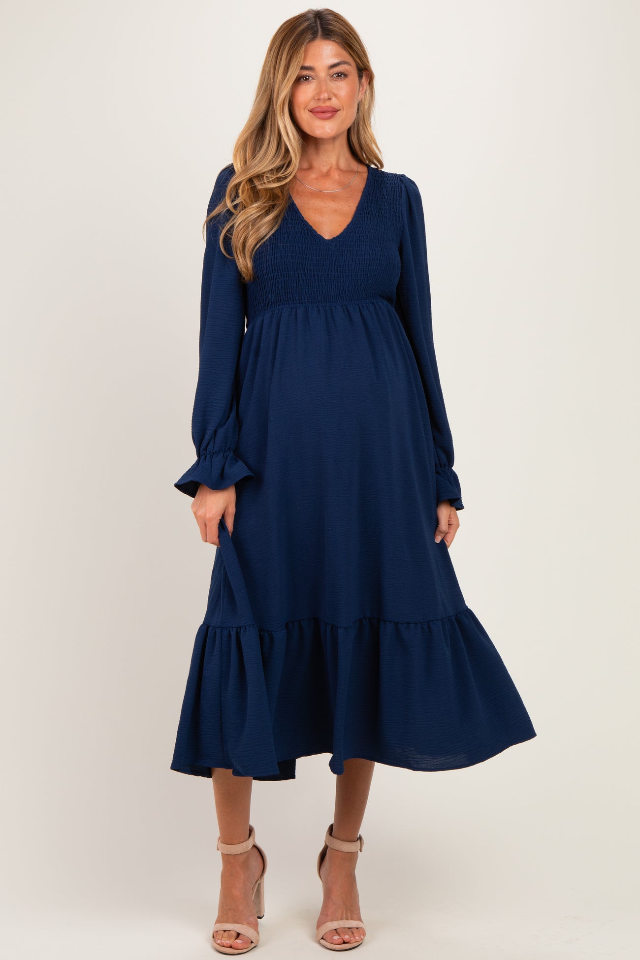 woman wearing a navy blue maternity dress with a smocked bodice and ruffled hem, showcasing her baby bump