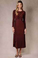 woman wearing a burgundy long sleeve wrap dress with a draped front and fitted silhouette