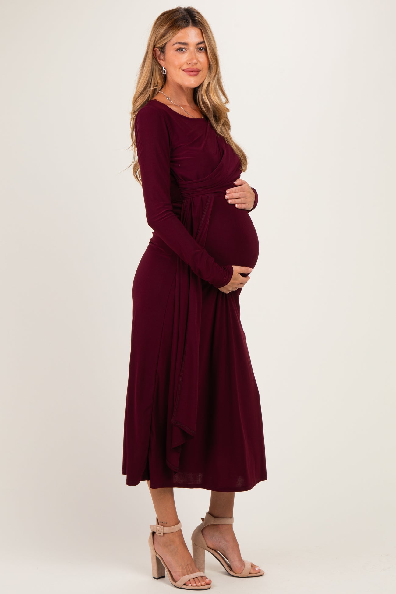 woman wearing a burgundy long sleeve maternity dress and holding her baby bump