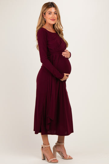 woman wearing a burgundy long sleeve maternity dress and holding her baby bump