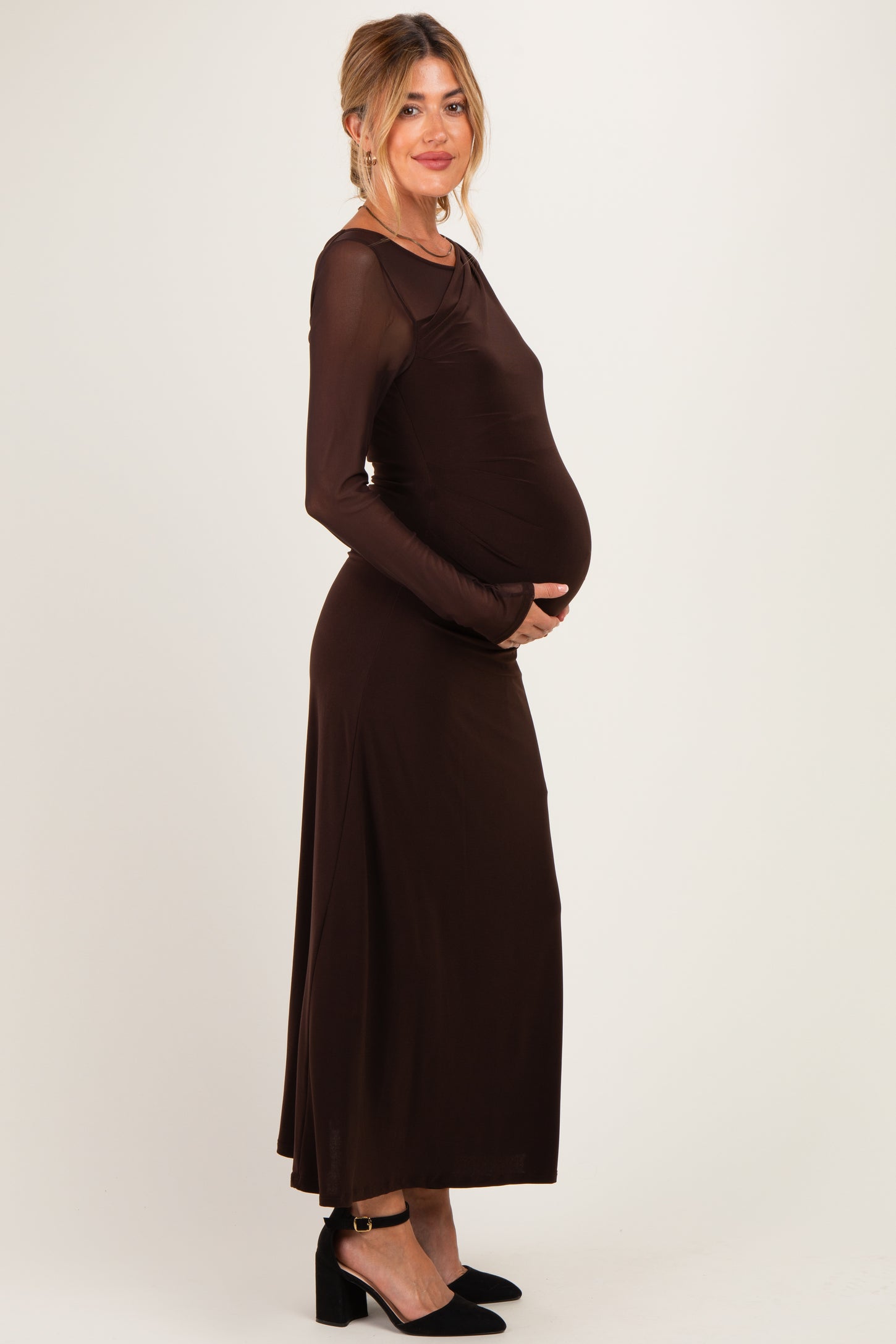 woman wearing a brown long sleeve maternity dress, cradling her baby bump