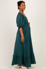 woman wearing a teal maternity maxi dress with puff sleeves and a ruffled hem, showcasing her baby bump