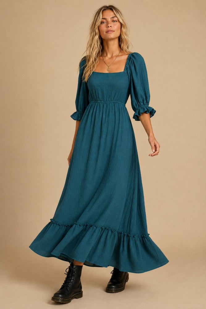 woman wearing a teal maxi dress with puff sleeves and a flounced hem, styled with black ankle boots