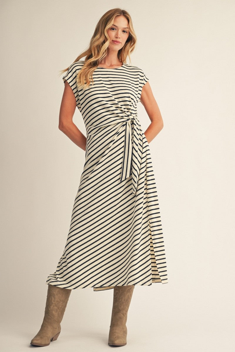 woman wearing a cream and black striped midi dress with a side tie and slit, paired with brown knee-high boots