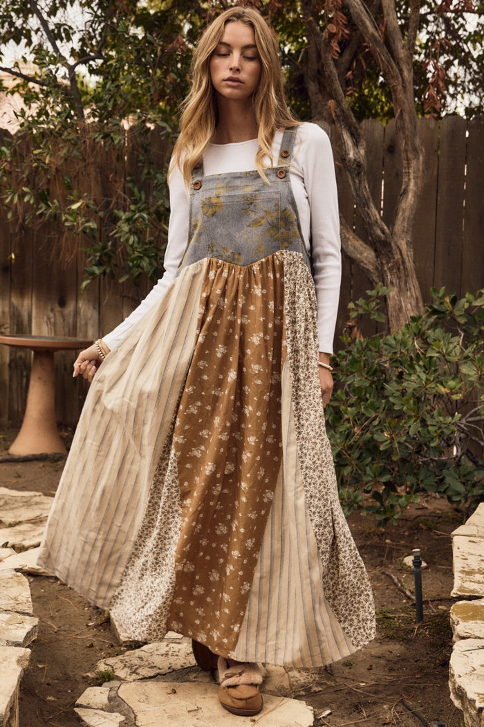 woman wearing a bohemian-style long patchwork dress with suspenders, featuring floral and striped patterns in earth tones