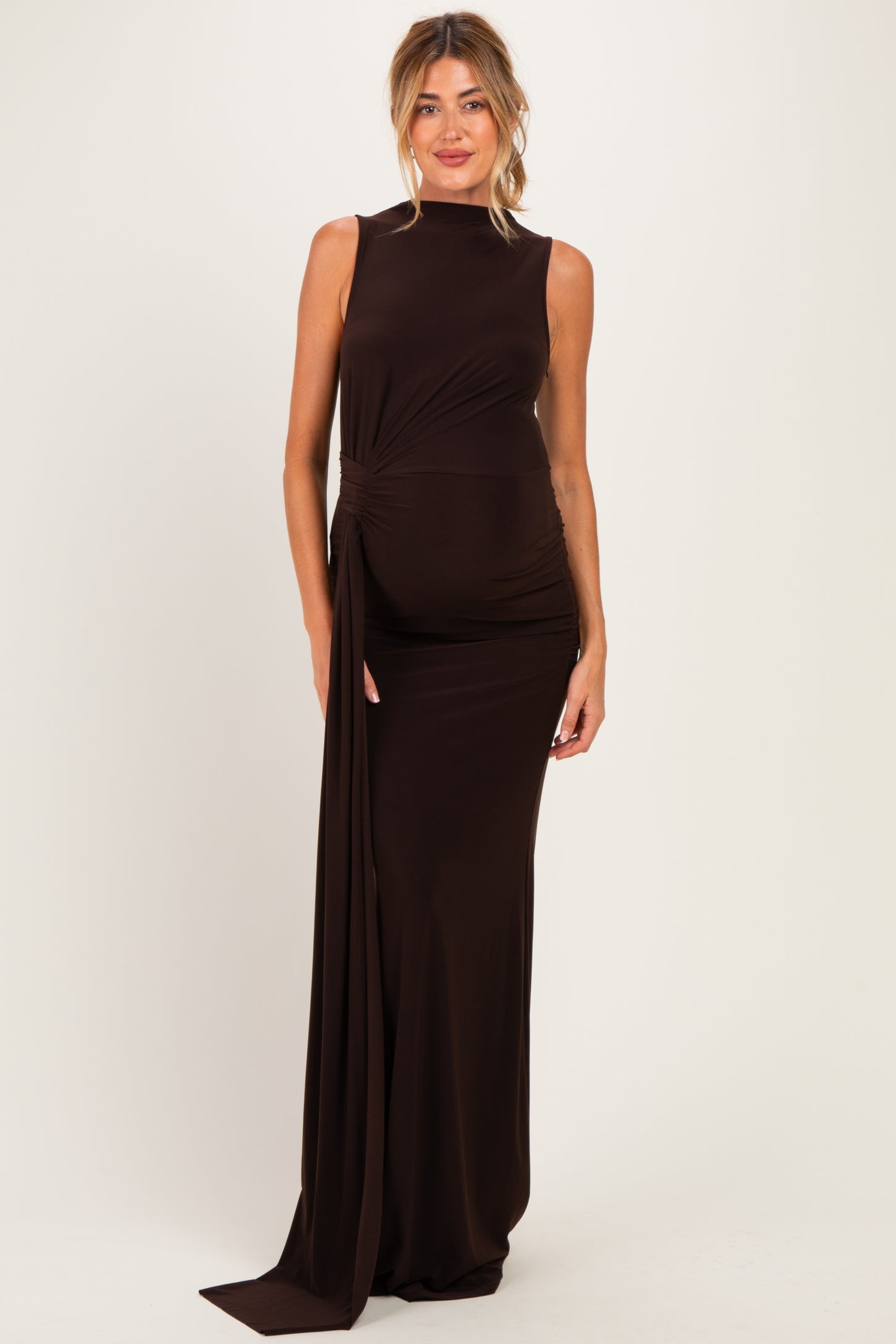 woman wearing a brown sleeveless maternity gown with a side drape and a visible baby bump