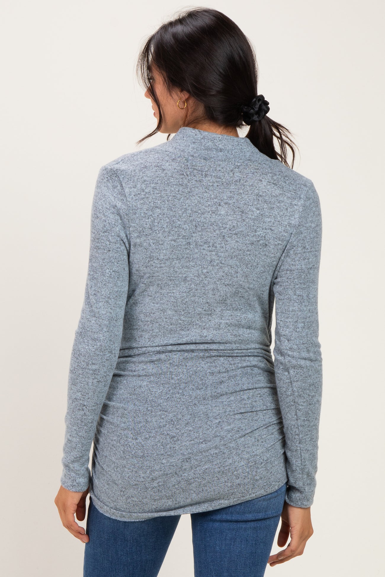 woman wearing a light gray long sleeve top with a relaxed fit and back ruching, styled with blue jeans
