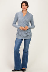 woman wearing a gray wrap-style long sleeve top and flared jeans, standing against a light background