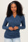 woman wearing a dark blue wrap long sleeve top with gathered side detailing and standing with hands clasped