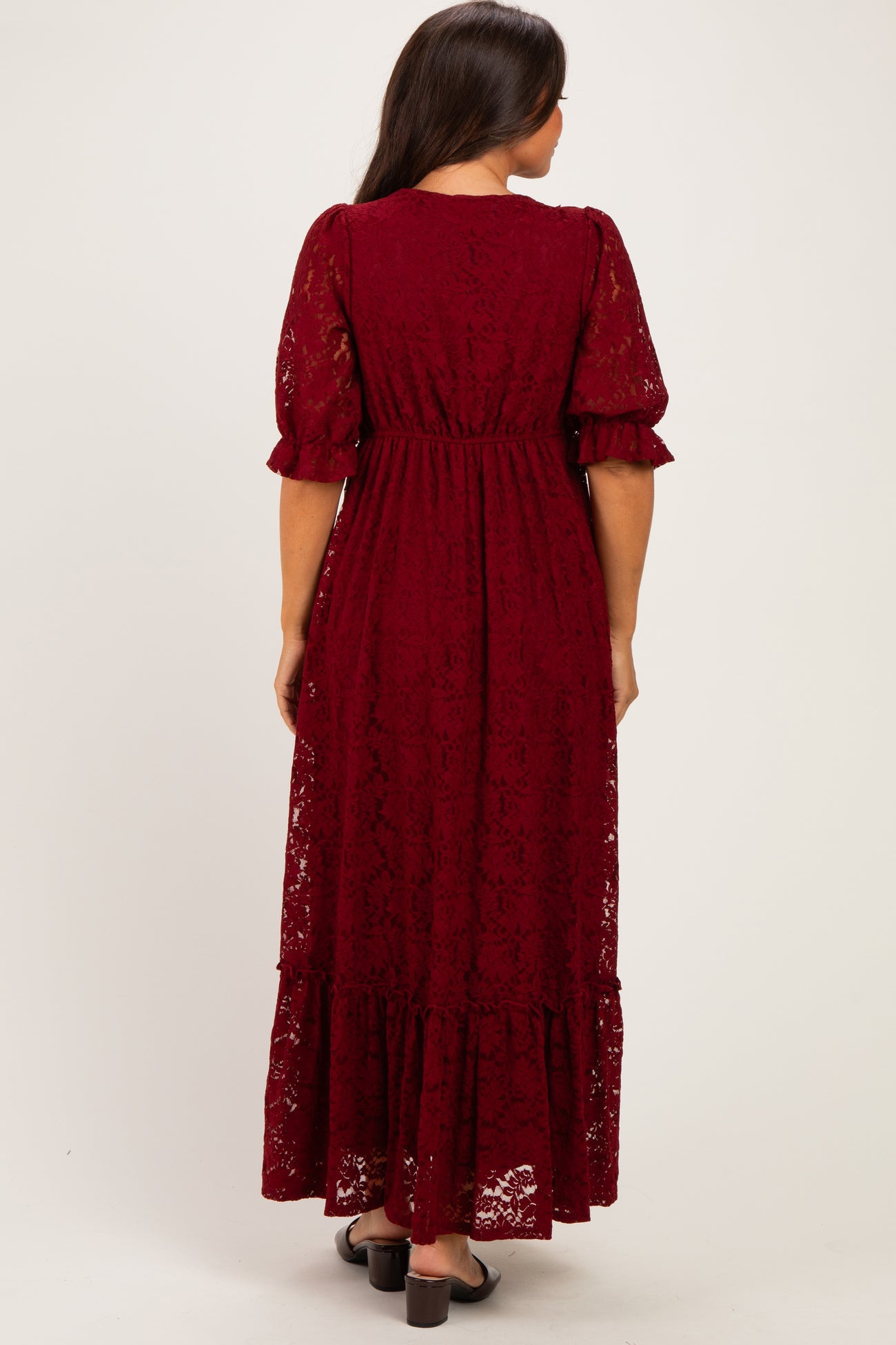woman wearing a burgundy lace maternity maxi dress with short puff sleeves and a tiered hem