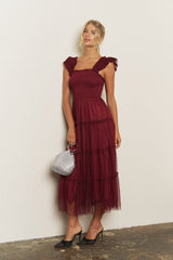 woman wearing a burgundy tiered maxi dress with ruffled straps and holding a sparkly silver handbag