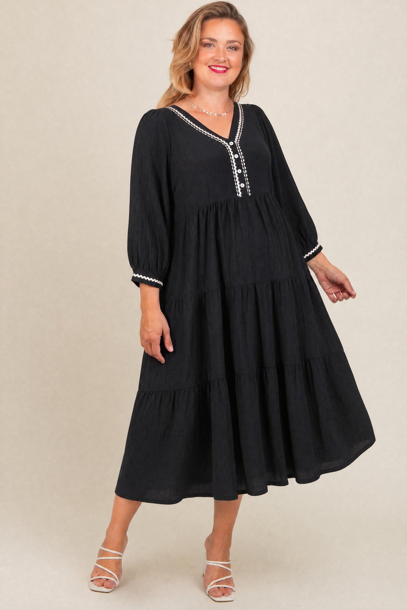 woman wearing a black maternity plus tiered dress with balloon sleeves and decorative buttons