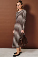 woman wearing a brown and cream striped long sleeve dress, holding a brown handbag, standing against a brown background