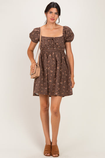 woman wearing a brown floral puff sleeve mini dress and holding a small handbag with a quilted design