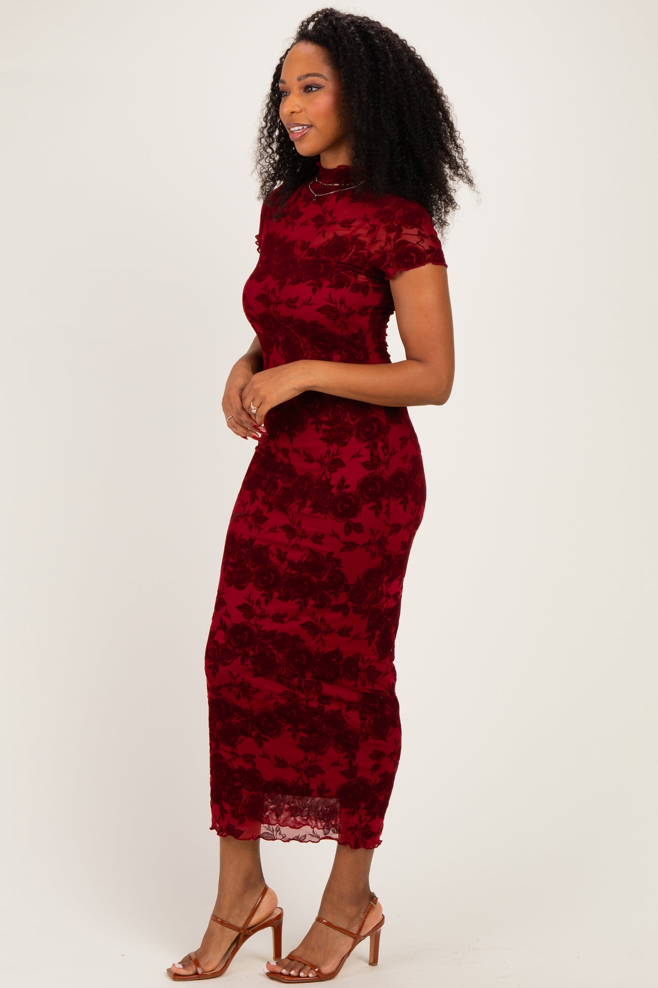 woman wearing a burgundy lace midi dress with short sleeves and floral pattern, standing sideways