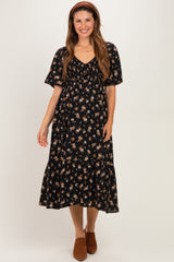 woman wearing a black floral maternity dress with short sleeves and a tiered skirt, smiling and standing with hands on her belly