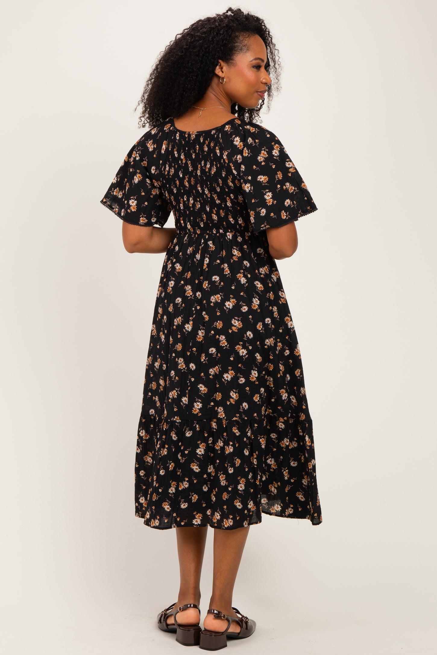 woman wearing a black floral midi dress with short flutter sleeves and a tiered skirt, shown from the back
