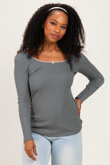 woman wearing a gray long sleeve top with a square neckline and a decorative detail, paired with light blue jeans