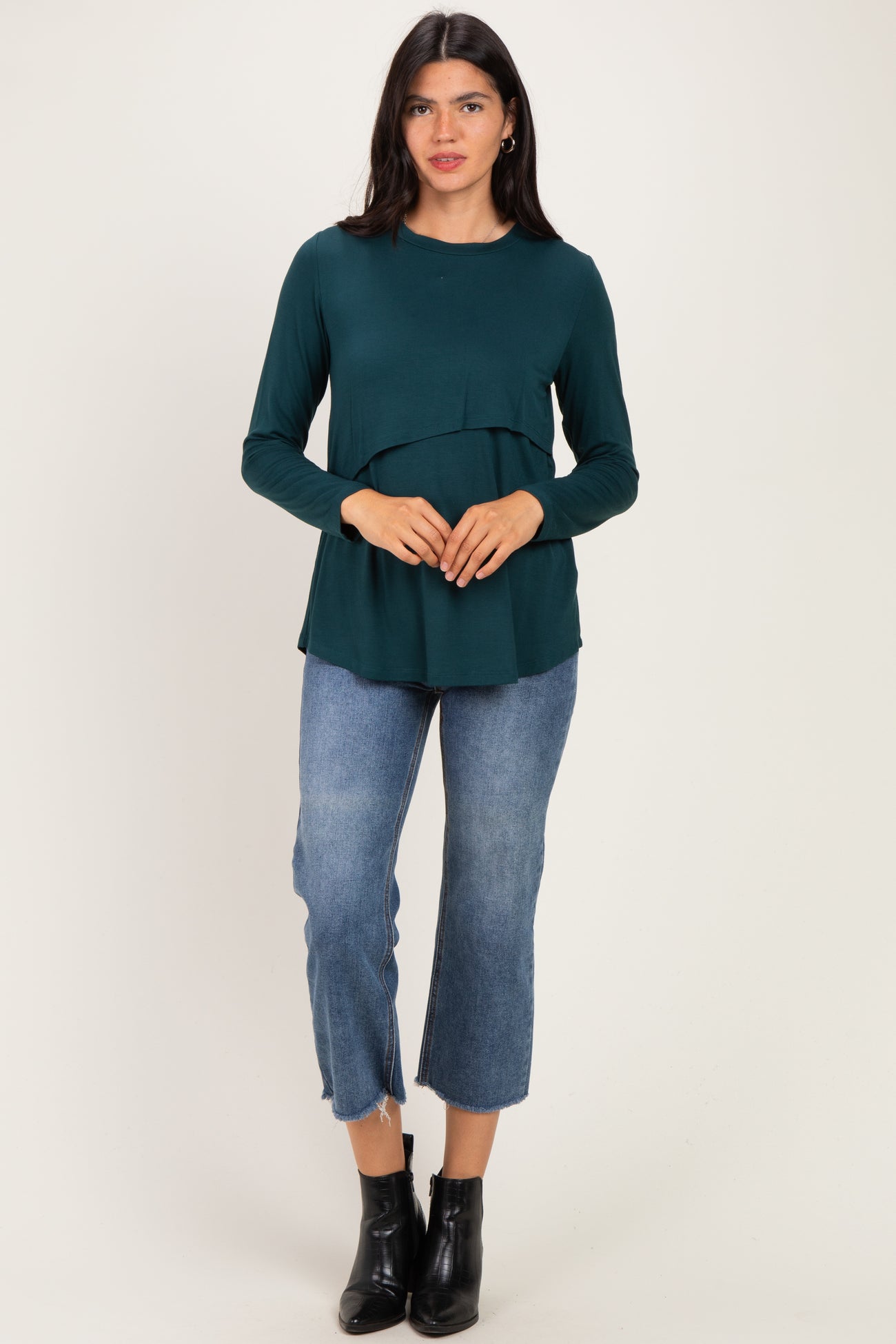 woman wearing a dark green long sleeve top with a tiered design and blue cropped jeans