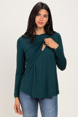 woman wearing a dark teal long sleeve top with a draped design and a keyhole detail at the chest, paired with jeans