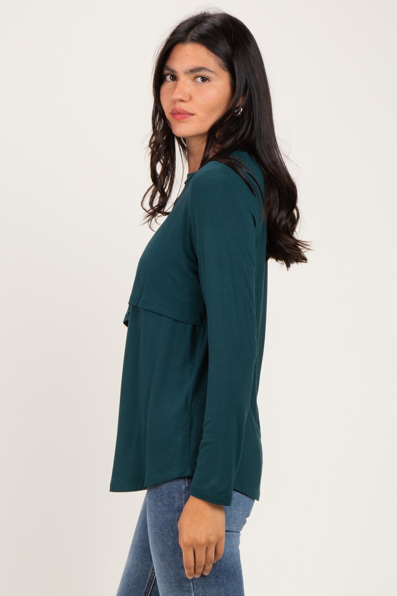 woman wearing a dark green long sleeve top with a layered design and a relaxed fit, paired with blue jeans