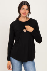 woman wearing a black long sleeve top with a keyhole cutout and layered front detail, styled with light blue jeans