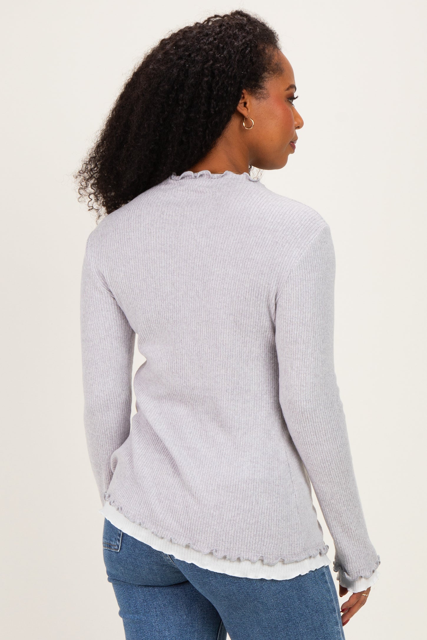woman wearing a light gray ribbed sweater with frayed edges and back view showing long sleeves and a relaxed fit