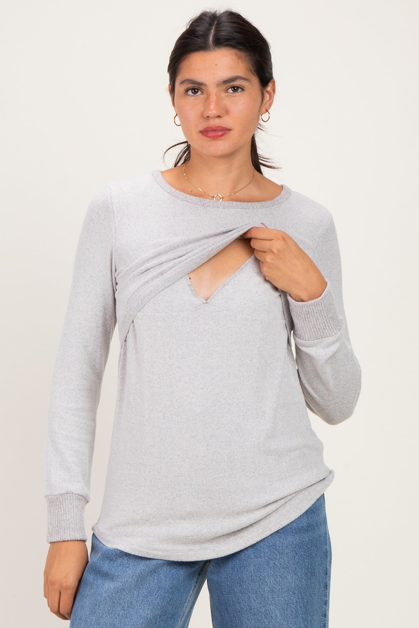 woman wearing a gray long sleeve top with a unique cutout detail, styled casually with blue jeans