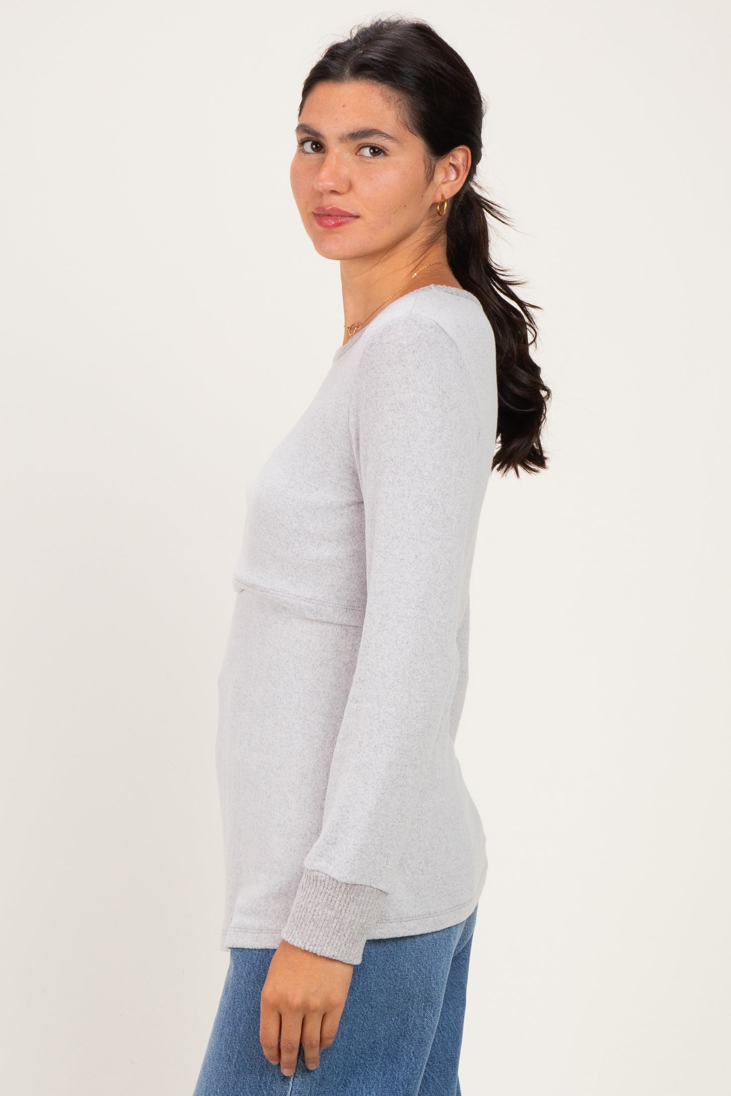 woman wearing a light gray long sleeve top with a fitted silhouette and side slits, paired with blue jeans