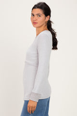 woman wearing a light gray long sleeve top with a fitted silhouette and side slits, paired with blue jeans