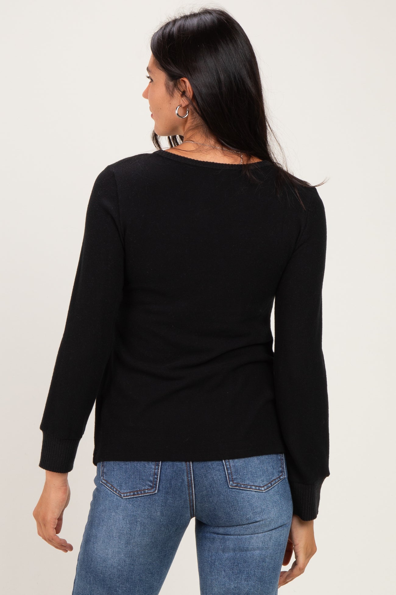 woman wearing a black long sleeve sweater with a fitted style and round neckline, seen from the back