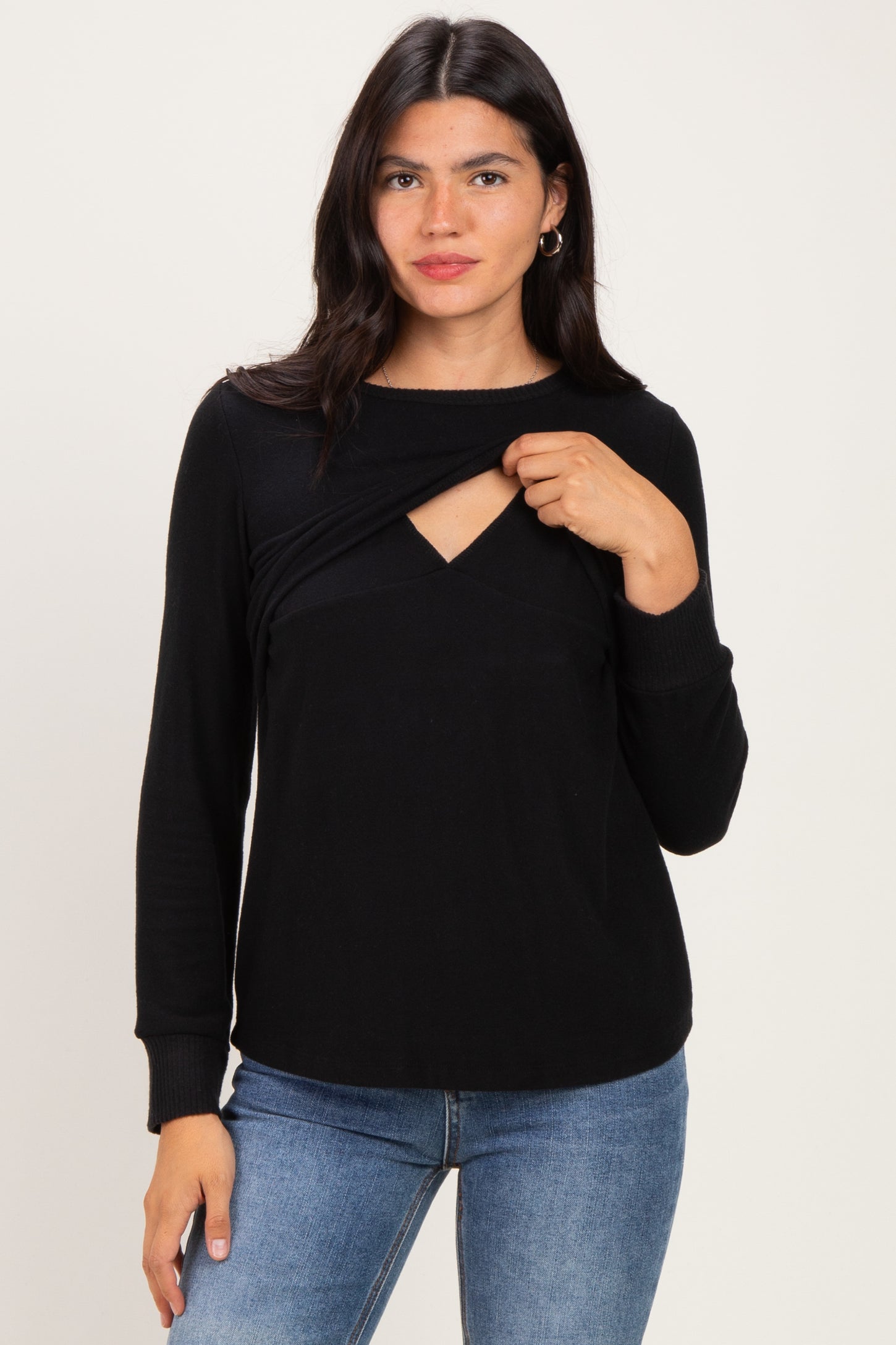 woman wearing a black long sleeve top with a twist front detail and a cut-out neckline, styled with blue jeans