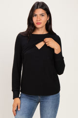 woman wearing a black long sleeve top with a twist front detail and a cut-out neckline, styled with blue jeans