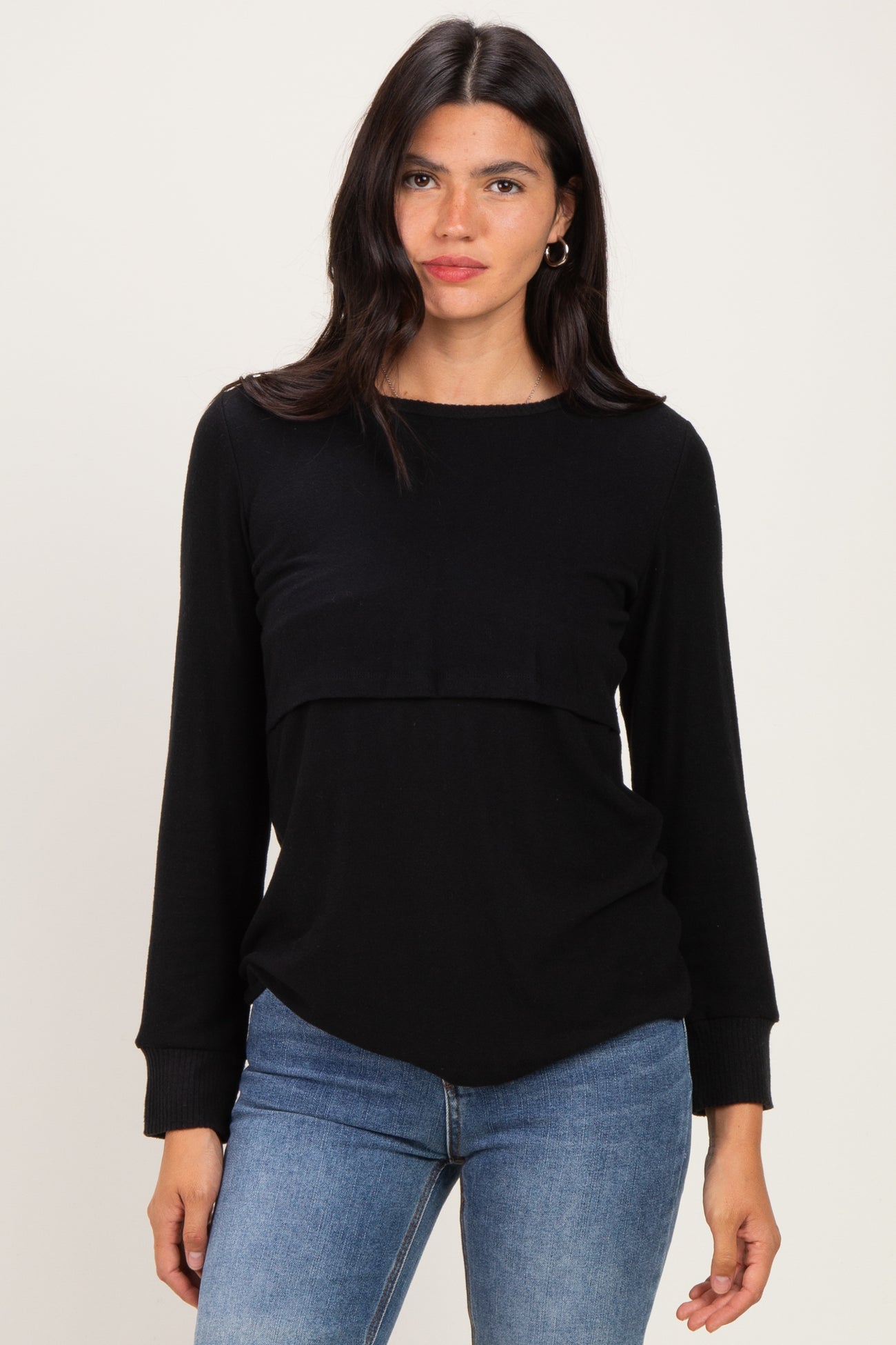 woman wearing a black long sleeve top with a layered design and relaxed fit, paired with blue jeans