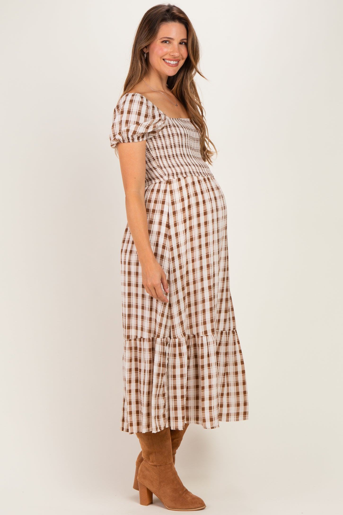woman wearing a brown and white checked maternity dress with a smocked bodice and tiered skirt, showing her baby bump