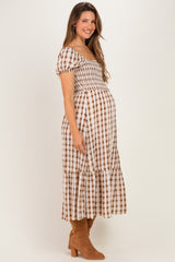 woman wearing a brown and white checked maternity dress with a smocked bodice and tiered skirt, showing her baby bump