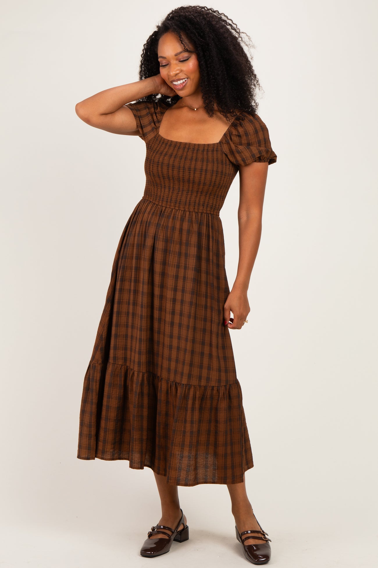 woman wearing a brown plaid midi dress with short puff sleeves and a tiered ruffle hem