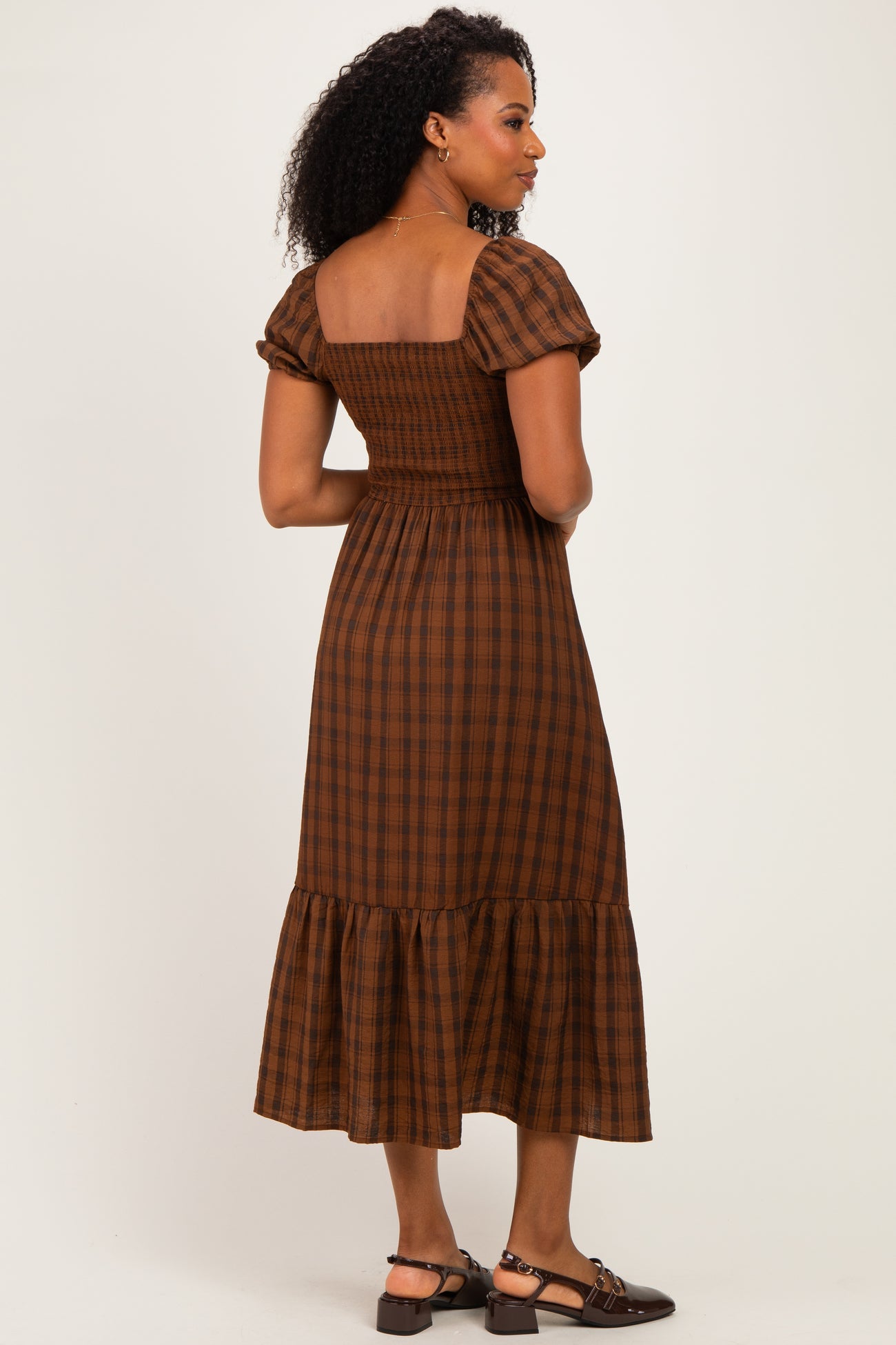 woman wearing a brown plaid puff sleeve midi dress with a smocked bodice and ruffled hem, viewed from the back