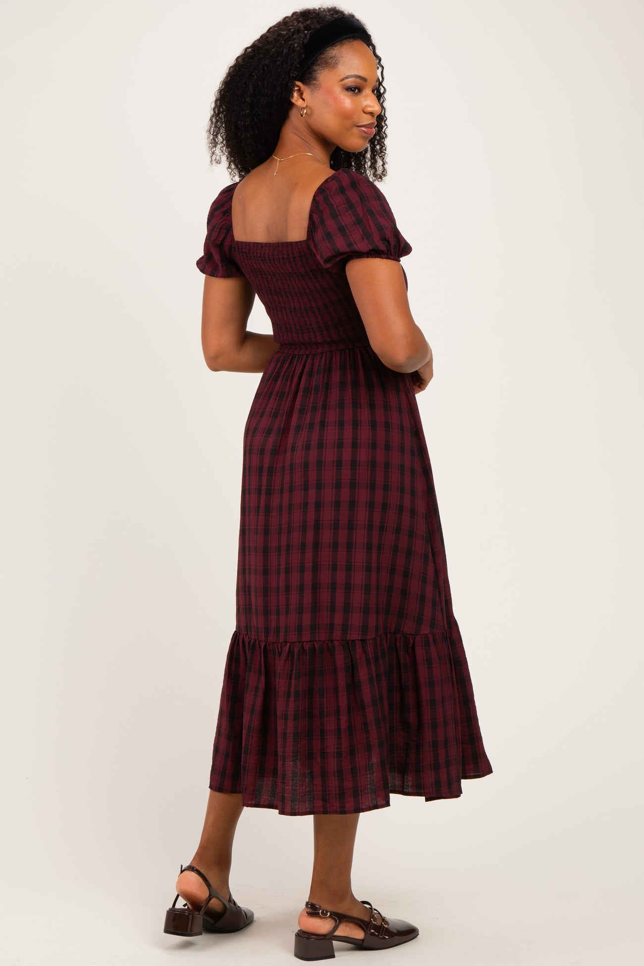 woman wearing a burgundy and black plaid midi dress with puff sleeves and a ruffled hem