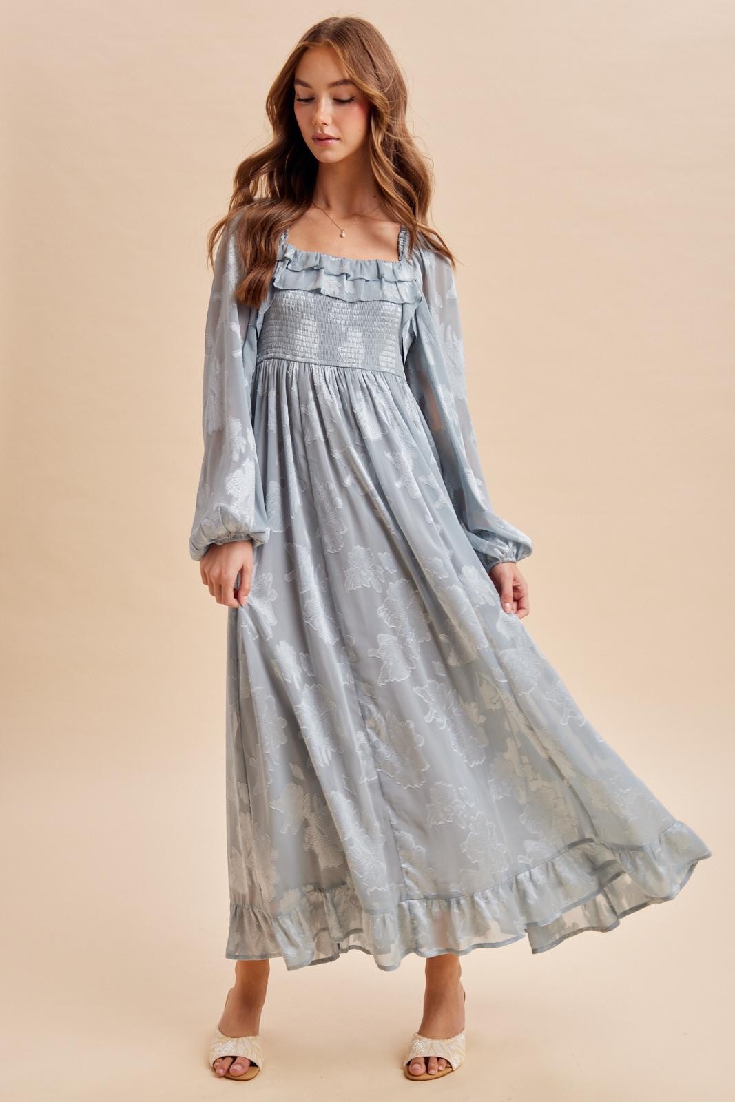 woman wearing a light blue long sleeve maxi dress with ruffle details and floral prints, posing with one hand on her hip