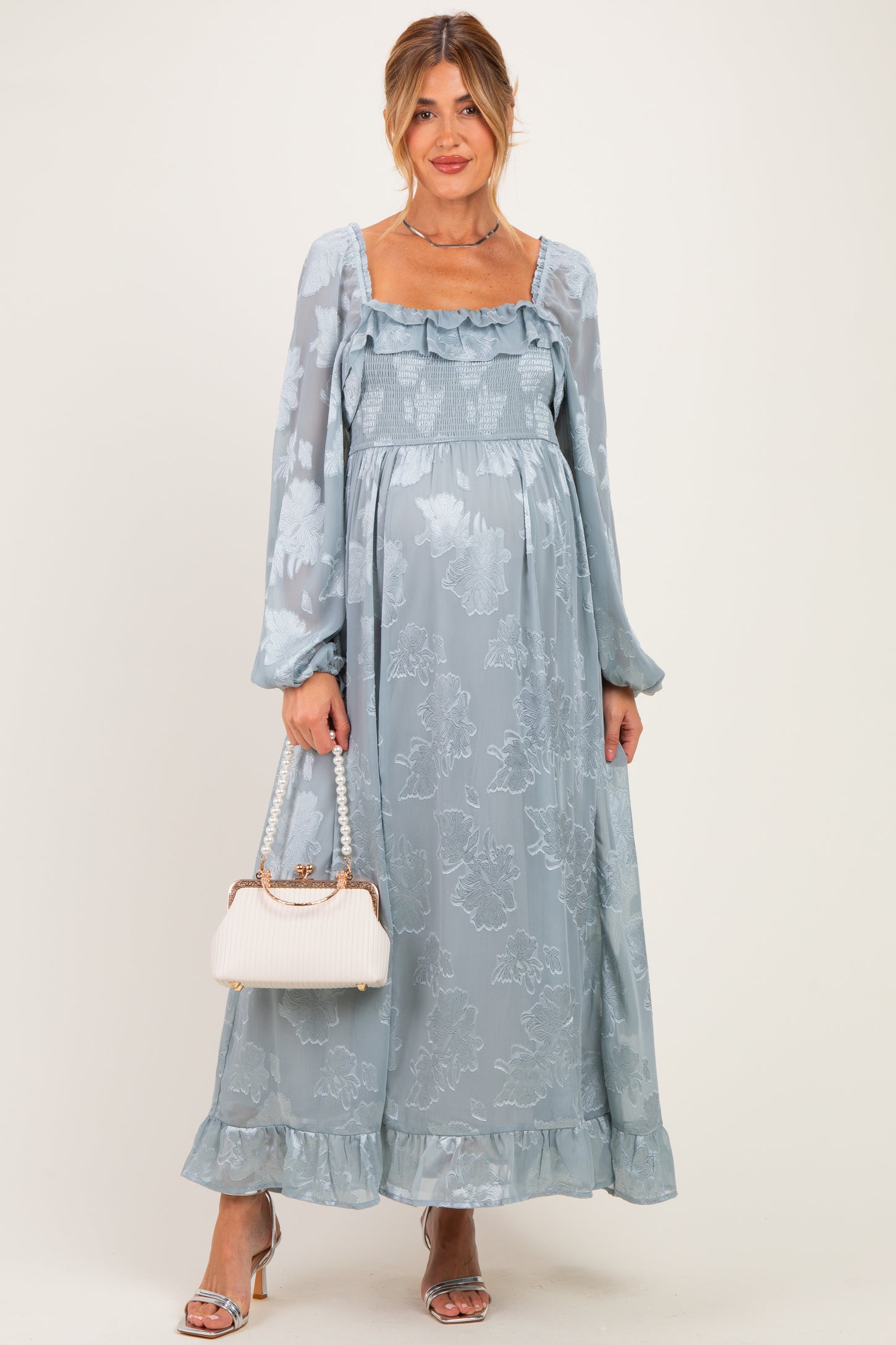 woman wearing a light blue floral maternity maxi dress with long sleeves and a baby bump, holding a handbag