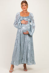 woman wearing a long light blue maternity dress with floral patterns and a smocked bodice, holding her baby bump