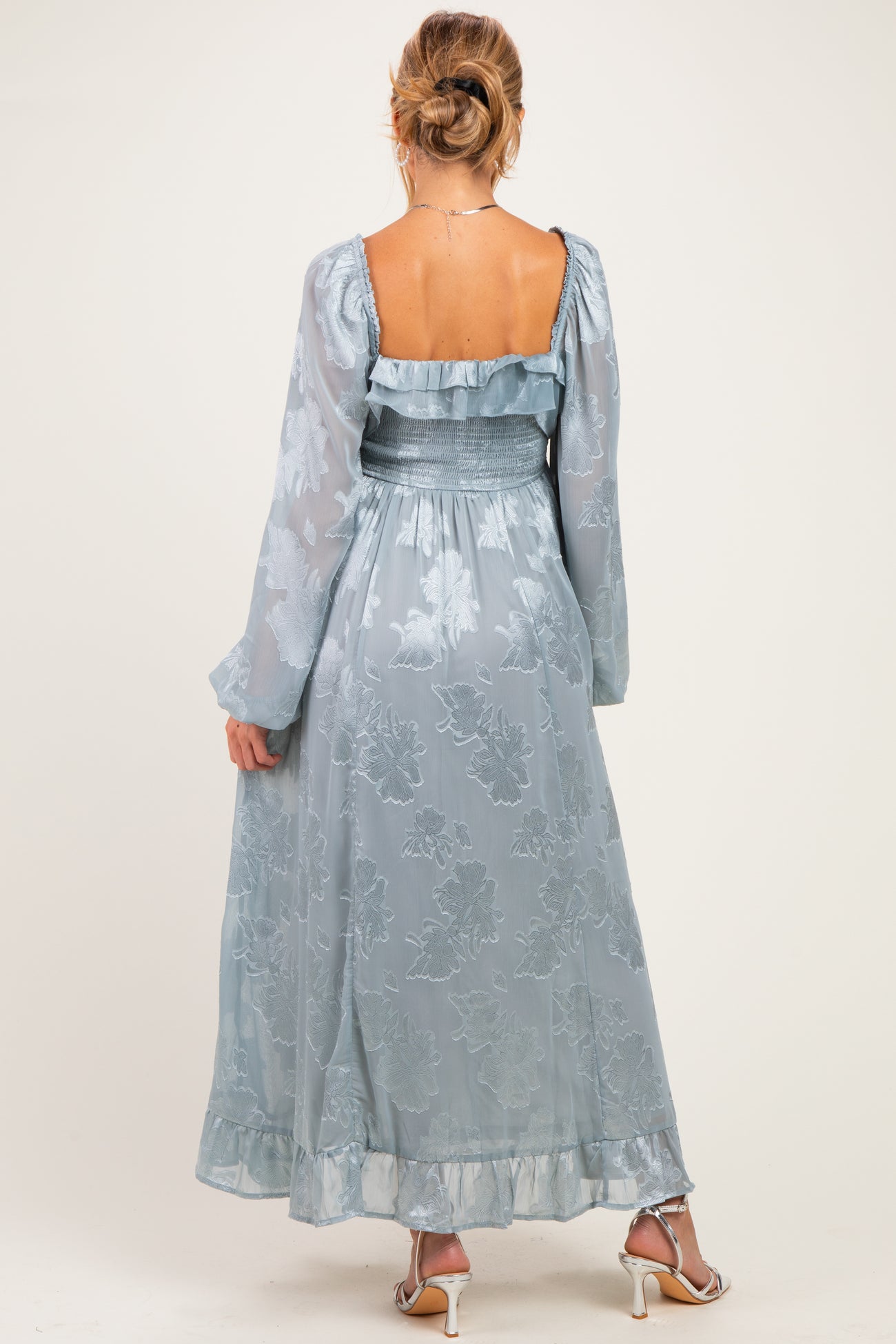 woman wearing a light blue floral maternity dress with long sleeves and smocked waist from the back