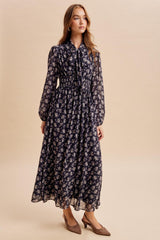 woman wearing a navy floral long sleeve maxi dress with a tie neck and smocked waist, styled with brown heels