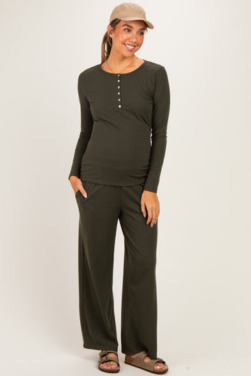 woman wearing a dark green long sleeve maternity top and matching pants, showcasing her baby bump